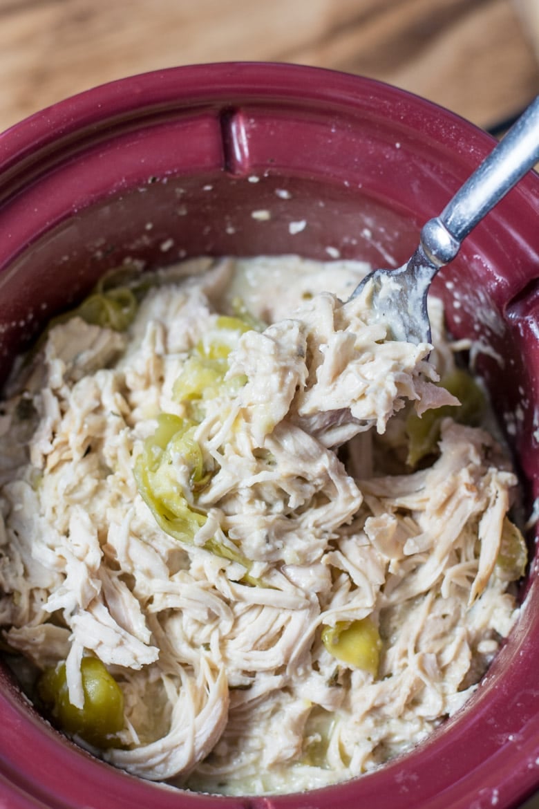 Shredded ranch chicken in a slow cooker with pepperoncini peppers, and a fork 
