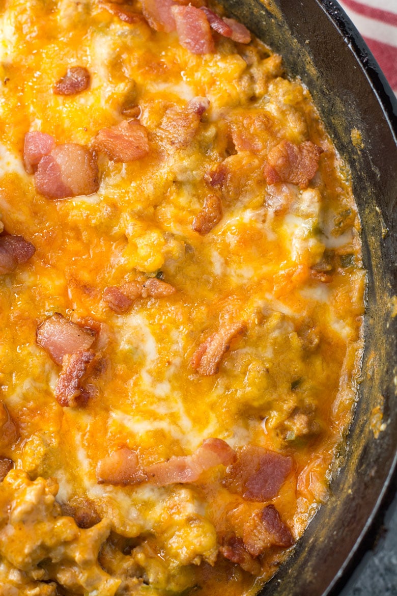 Overhead view of a cheeseburger casserole, topped with melted cheese and bacon, cooking in a skillet.