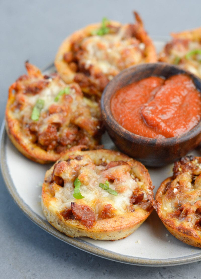 Overhead view of keto friendly pizza muffins on a white plate with a dish of marinara sauce in the middle. 