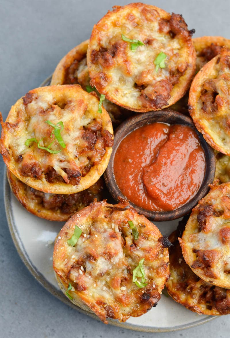 Overhead view of pizza muffins on a white plate with a dish of marinara sauce in the middle. 