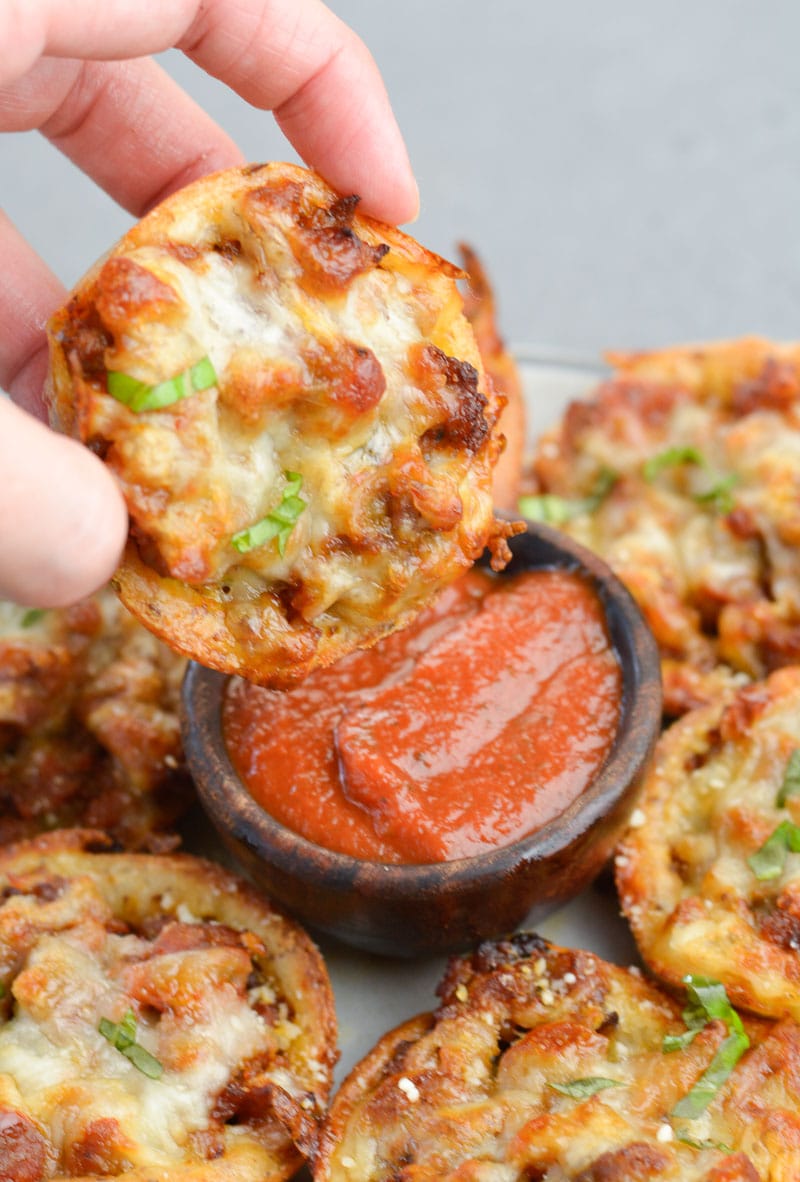 A pizza muffin being dunked into a small bowl of marinara sauce. 