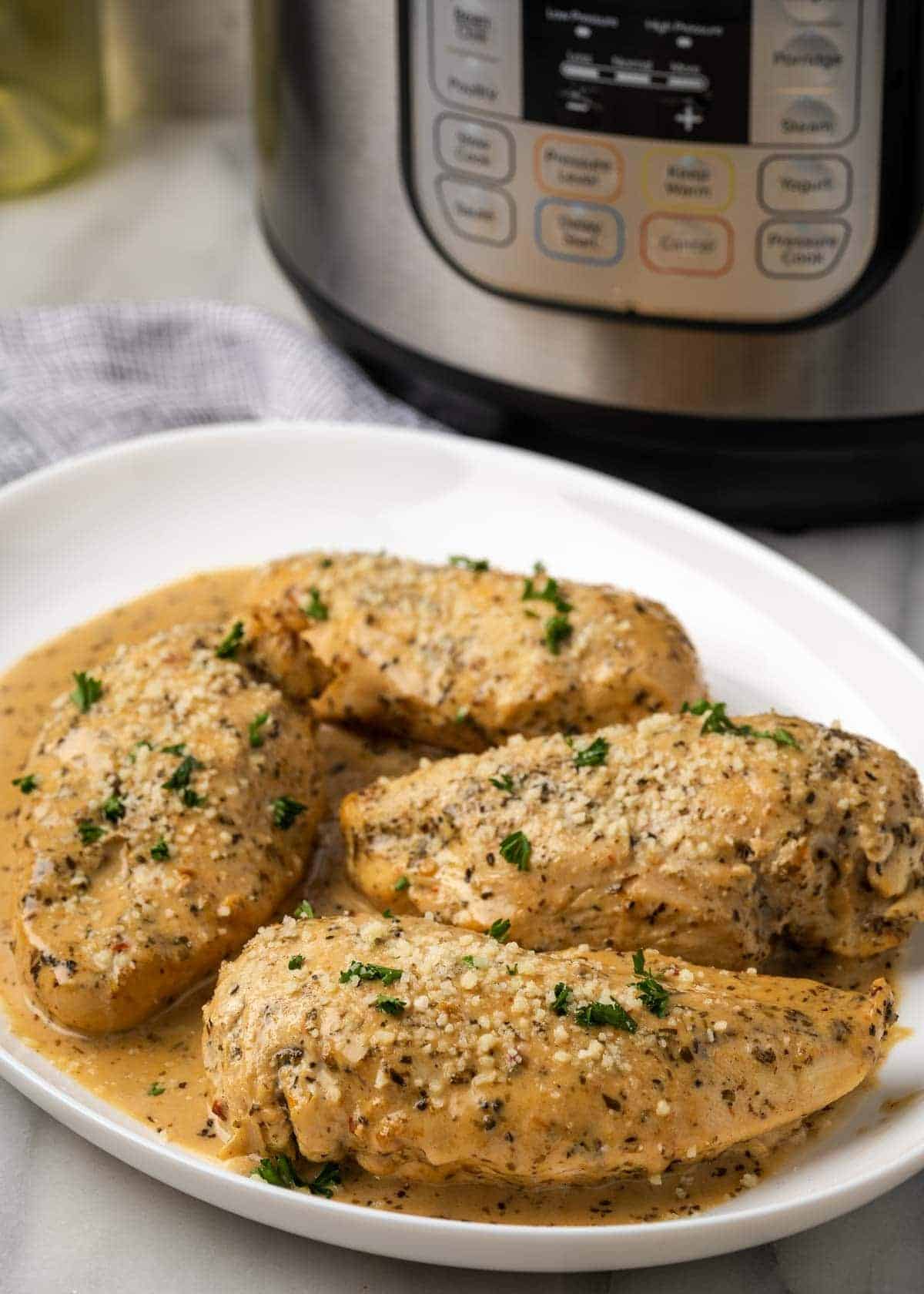A platter filled with four juicy chicken breasts covered in a parmesan cream sauce, all in front of an Instant Pot
