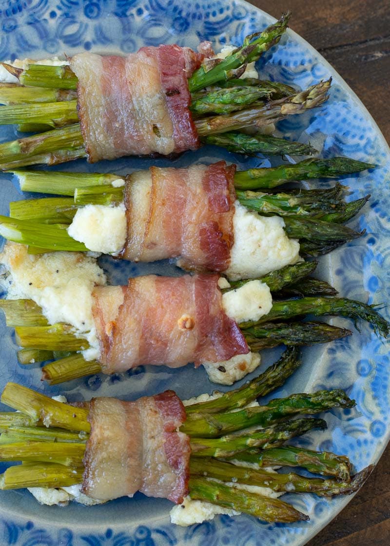 A plate with four bundles of baked asparagus and melty cheese wrapped in bacon