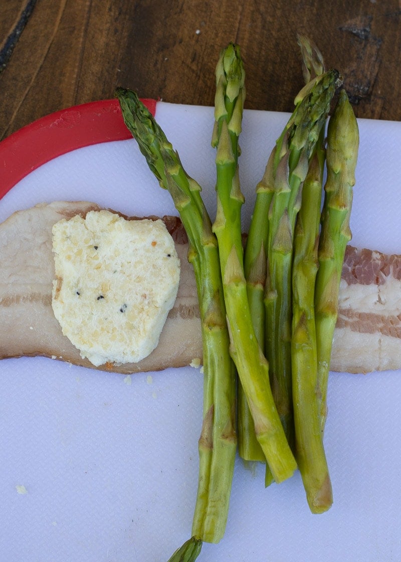 Six pieces of raw asparagus and a spoonful of cheese mixture on a piece of uncooked bacon