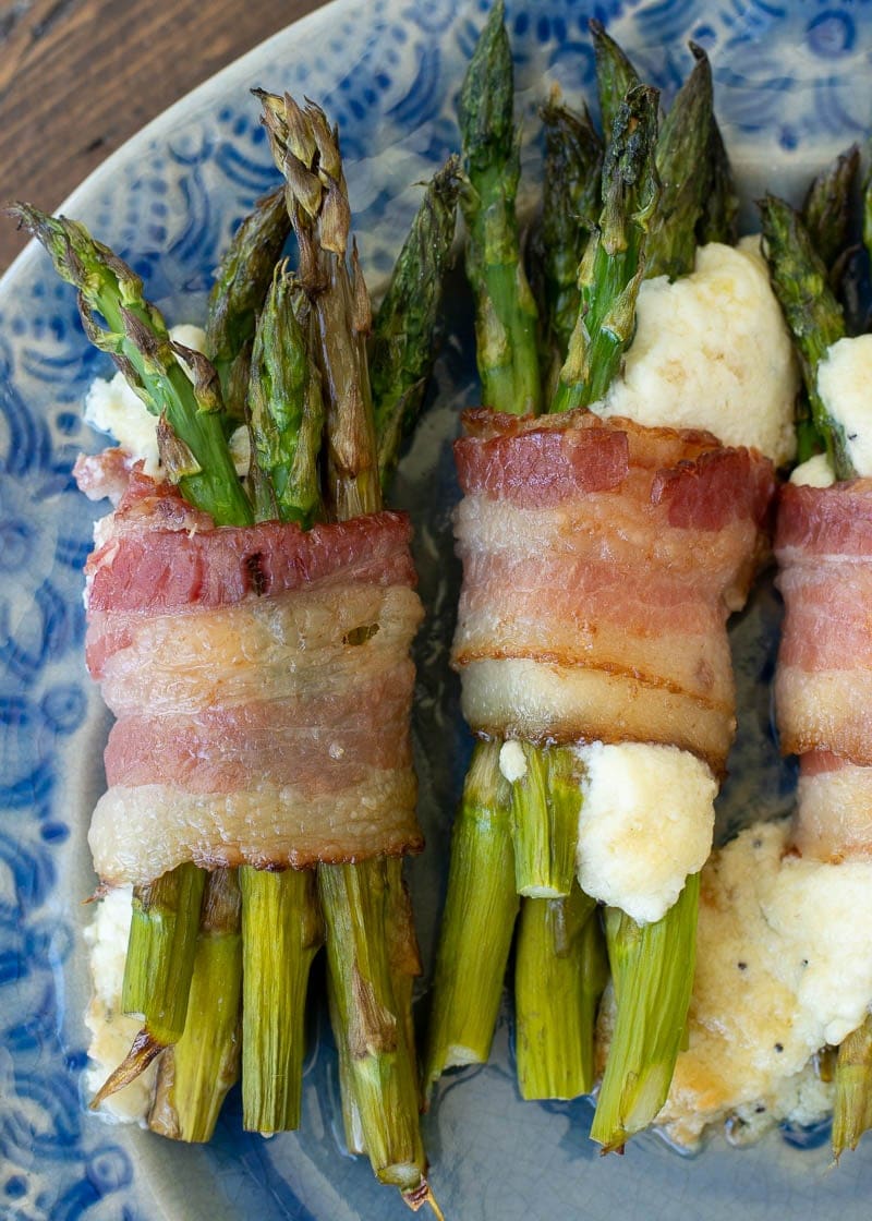 Two bundles of bacon wrapped asparagus with cheese on a plate