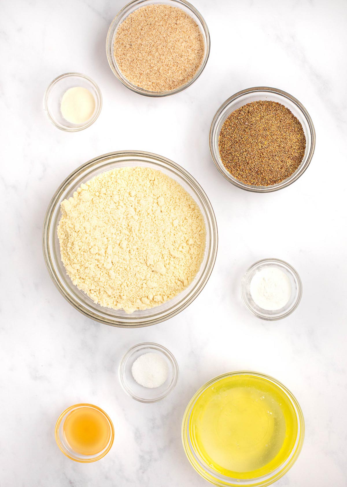 Overhead view of the ingredients needed for low carb bread: bowls of psyllium husk flakes, ground flaxseed meal, almond flour, sea salt, baking powder, xanthan gum, apple cider vinegar, and egg whites.