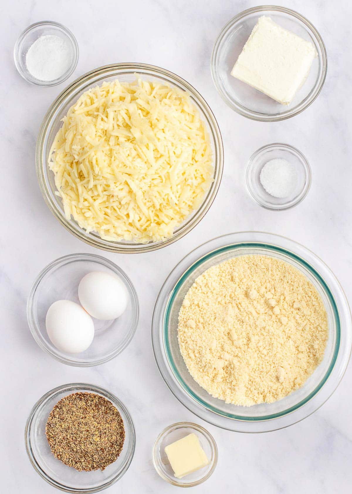 Overhead view of the ingredients needed for keto dinner rolls, in bowls: almond flour, flaxseed meal, shredded mozzarella cheese, whole eggs, cream cheese, butter, salt, and baking powder