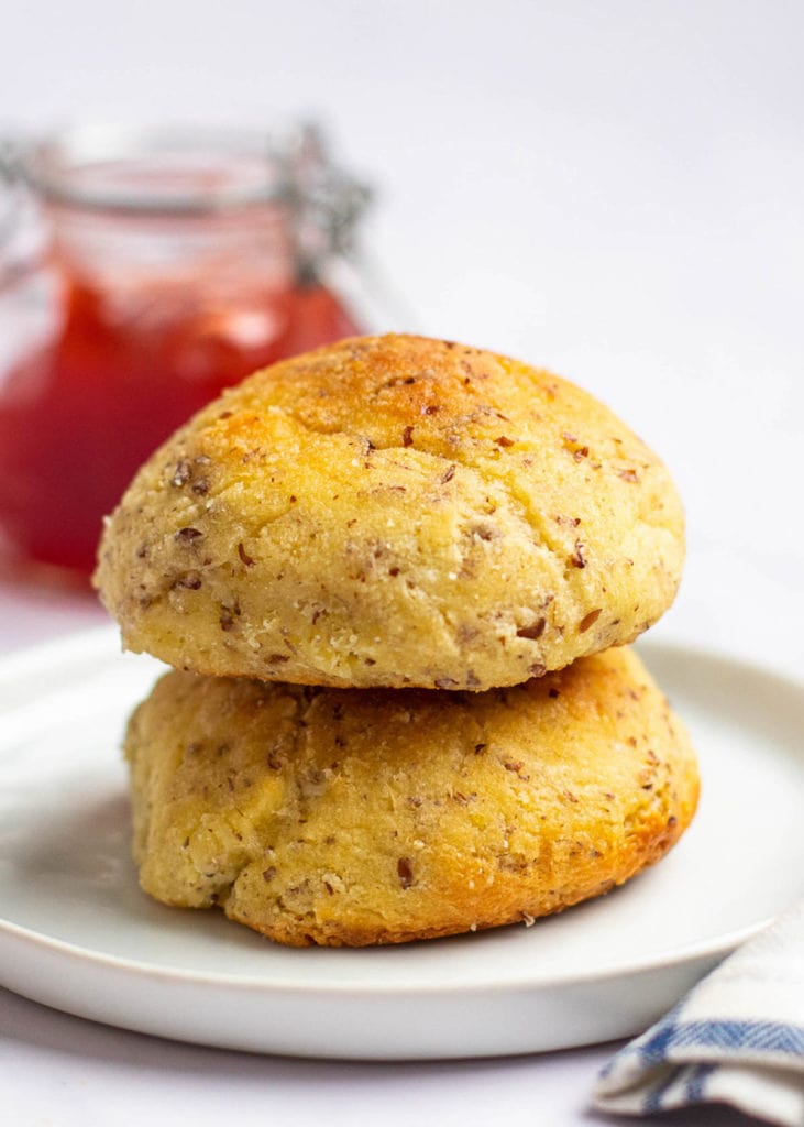 Two dinner rolls on top of each other on a plate, with a jar of jam in the background