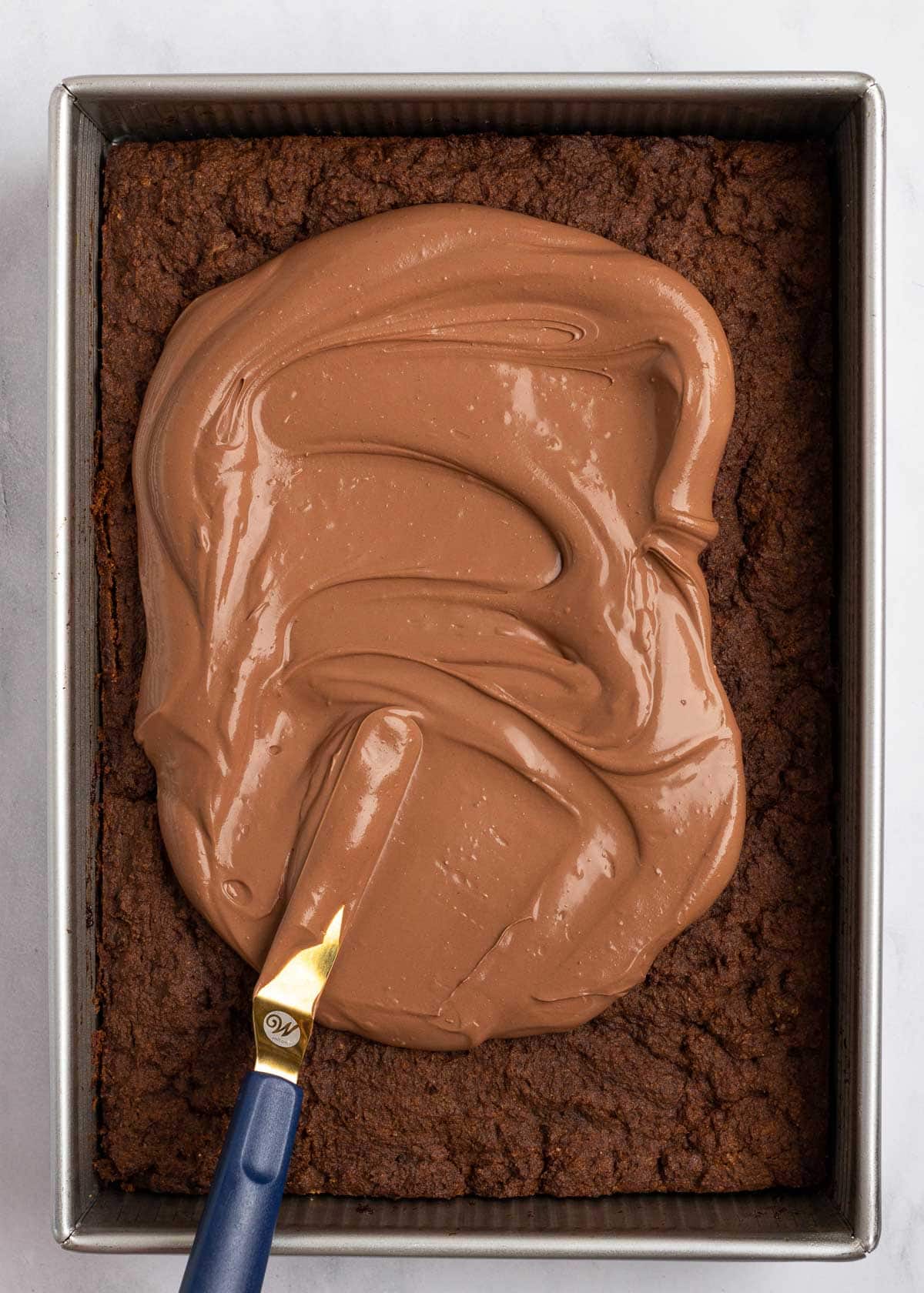An offset spatula evening out chocolate frosting on a chocolate cake