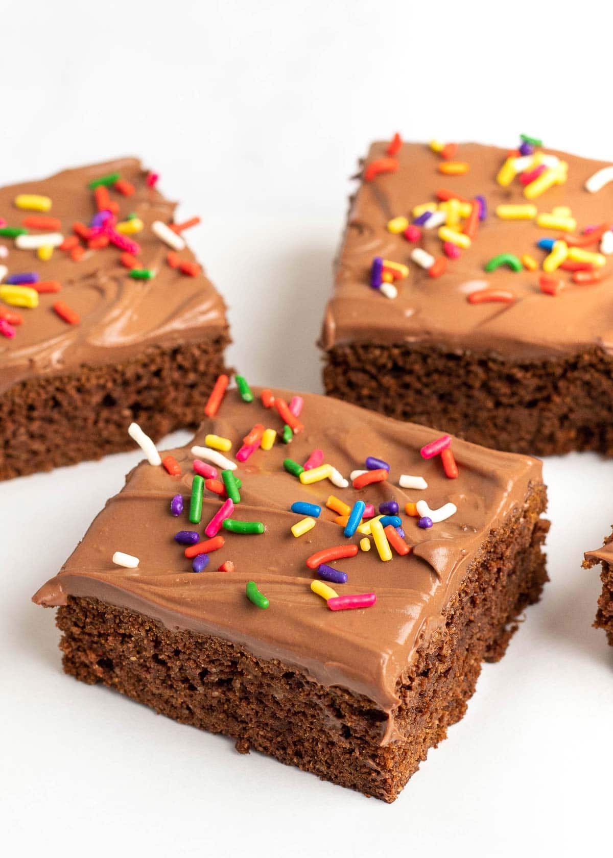 Three squares of chocolate cake covered with chocolate frosting and sprinkles