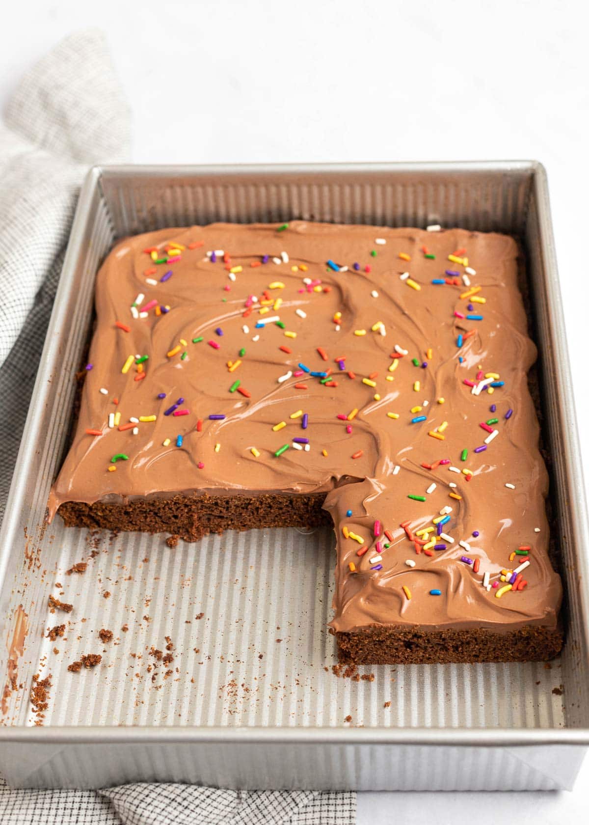 Chocolate cake in a cake pan, covered in sprinkles, with a few pieces cut out