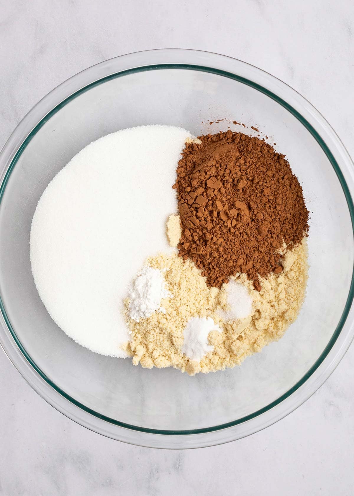A mixing bowl filled with almond flour, cocoa powder, monk fruit sweetener, salt, baking powder, and baking soda