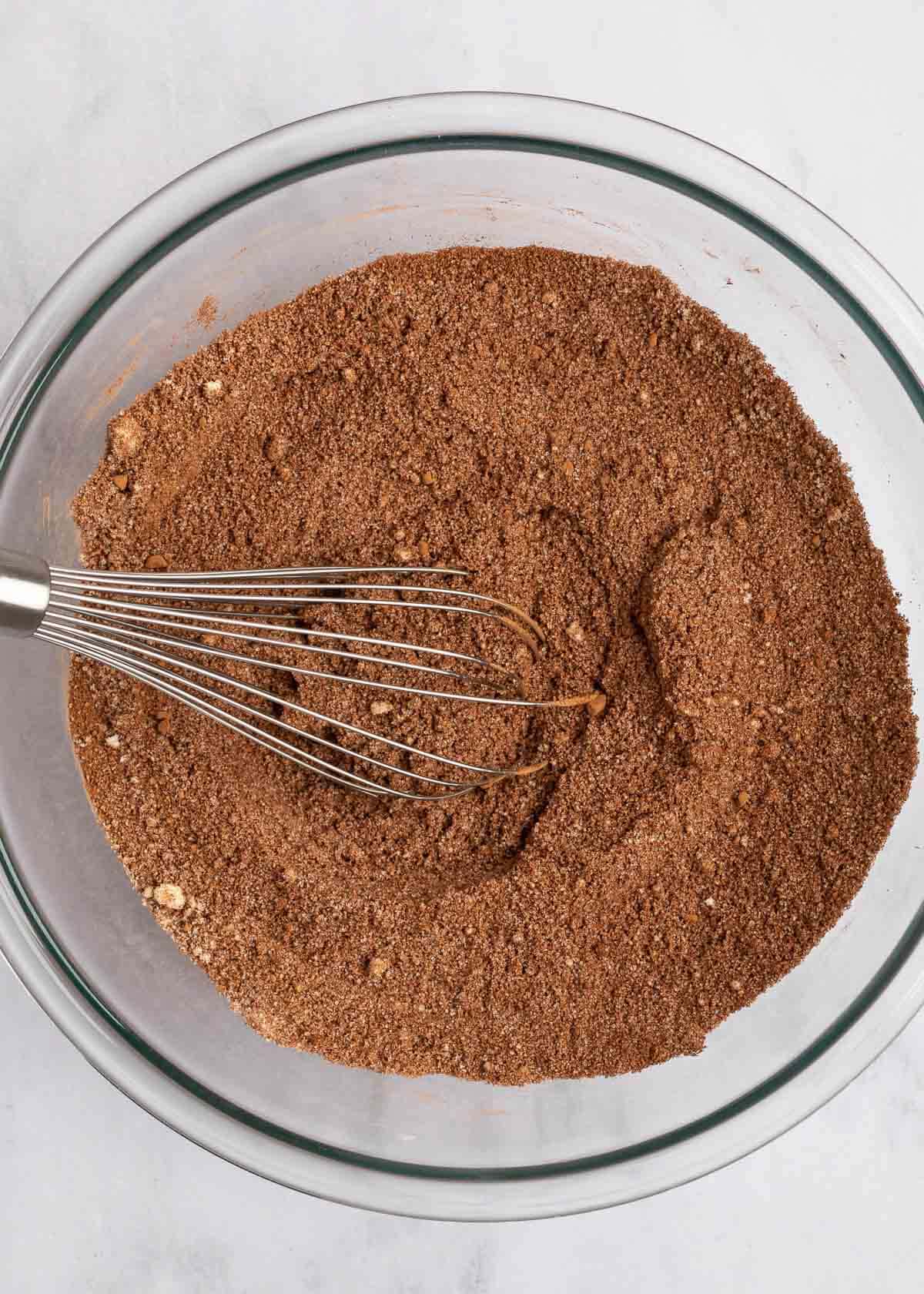 A mixing bowl with almond flour, cocoa powder, and other dry ingredients, and a whisk