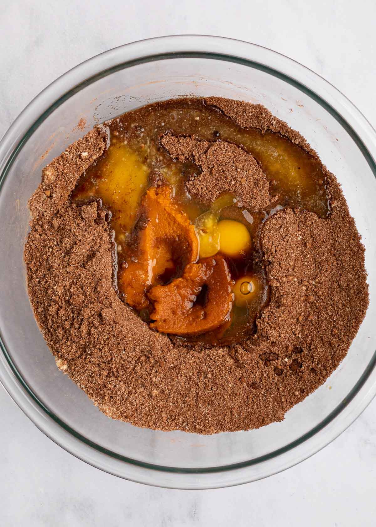 A bowl with cocoa powder and almond flour, with a well in it with eggs, pumpkin puree, and butter in it