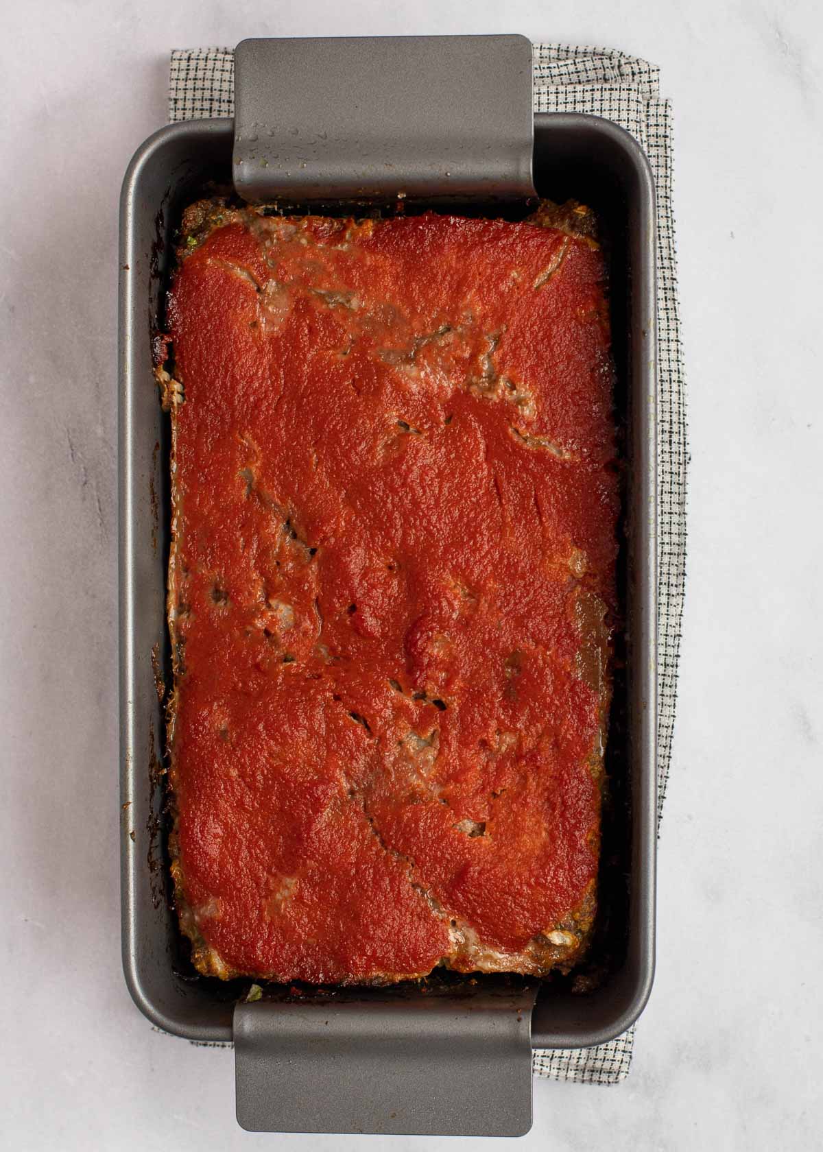 Overhead view of a baked meatloaf in a loaf pan, covered in sauce