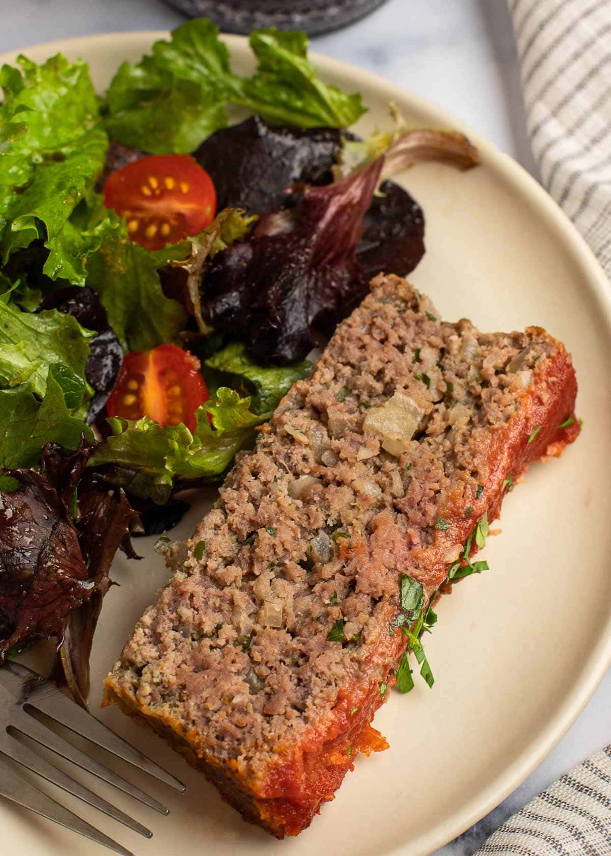 A piece of meatloaf on a plate next to a salad