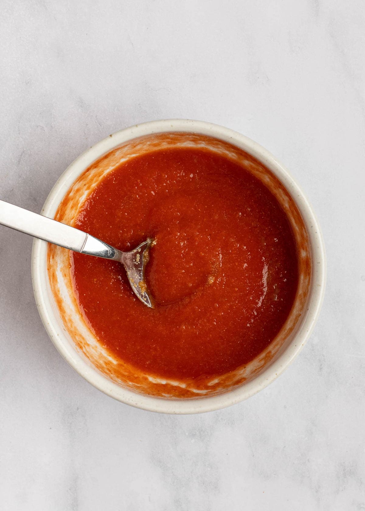 Overhead view of a bowl with a tomato-based sauce and a spoon in it