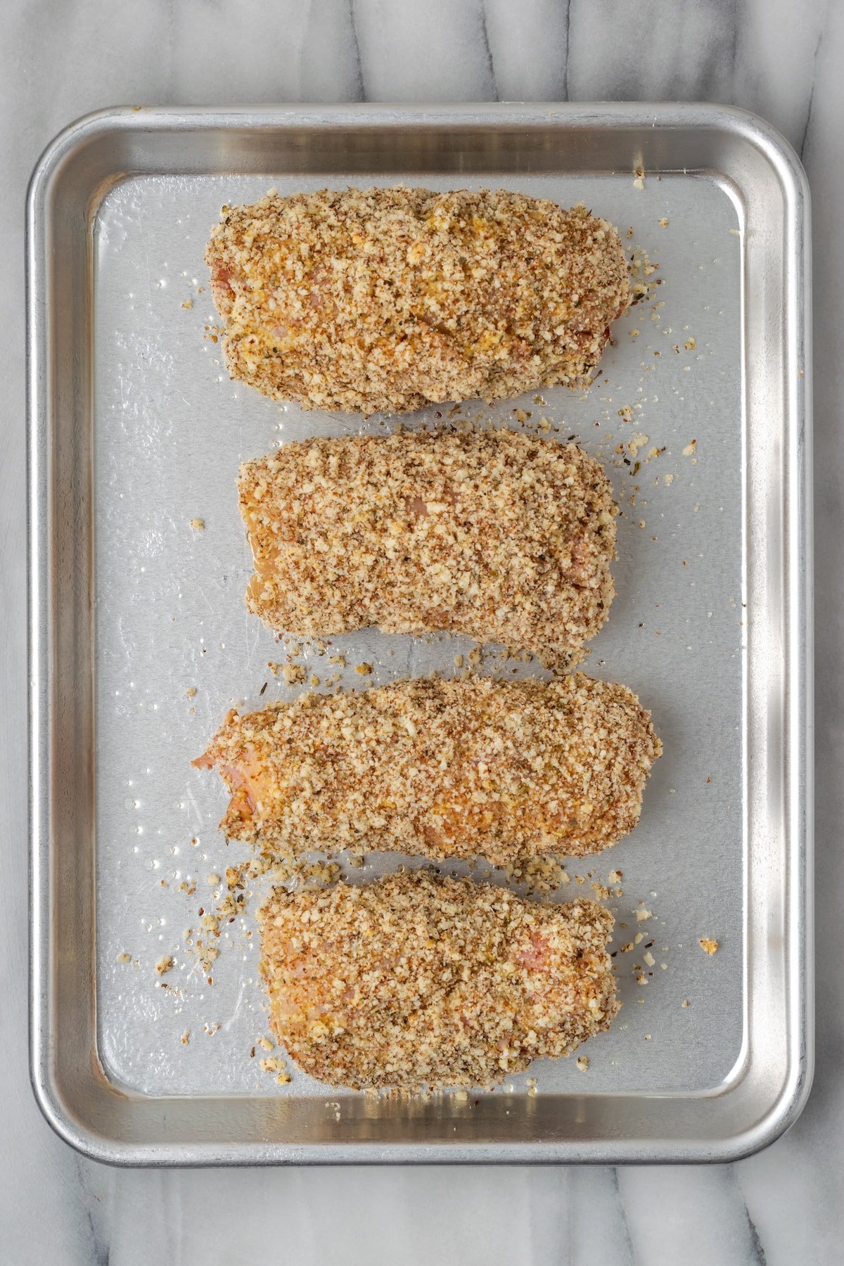 Overhead view of four breaded but unbaked chicken cordon bleus on a baking sheet