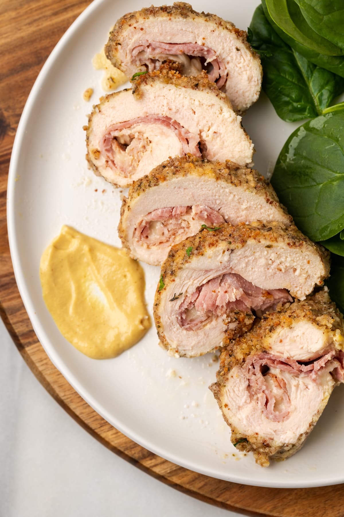 Overhead view of five slices of chicken cordon bleu on a plate with mustard and spinach