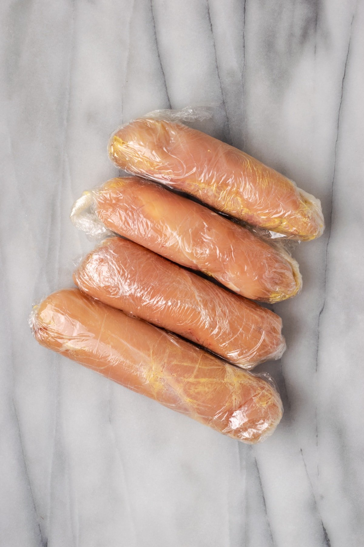 Four rolled up logs of stuffed chicken breasts, covered in plastic wrap