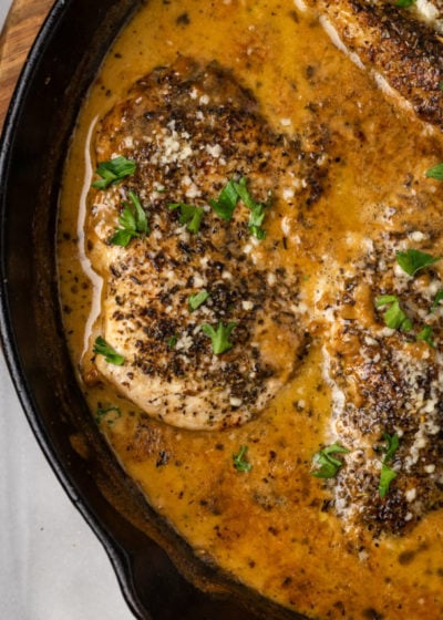 A close up of a chicken breast in a pot cooking in cream sauce