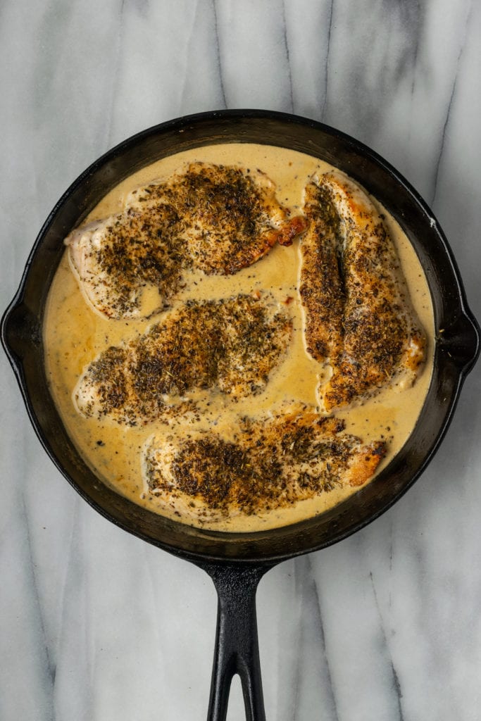 A skillet full of cream sauce with four chicken breasts in it