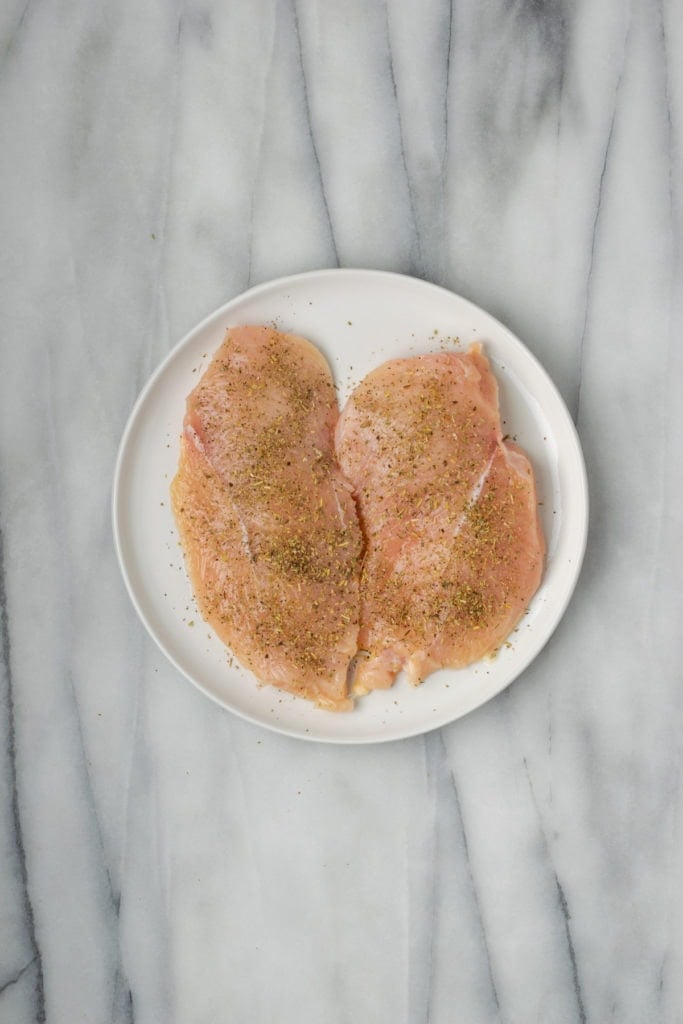 A plate with a chicken breast cut in half and seasoned