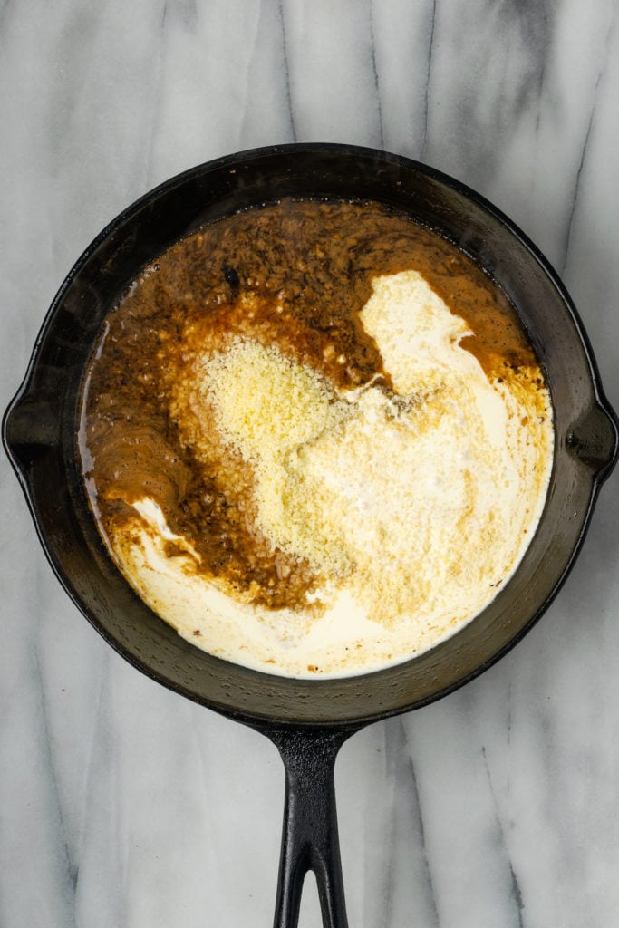 A skillet with wine, a pile of parmesan cheese, and some cream in it