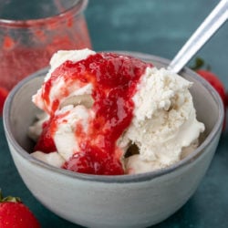 A bowl of ice cream topped with strawberry sauce, with a spoon