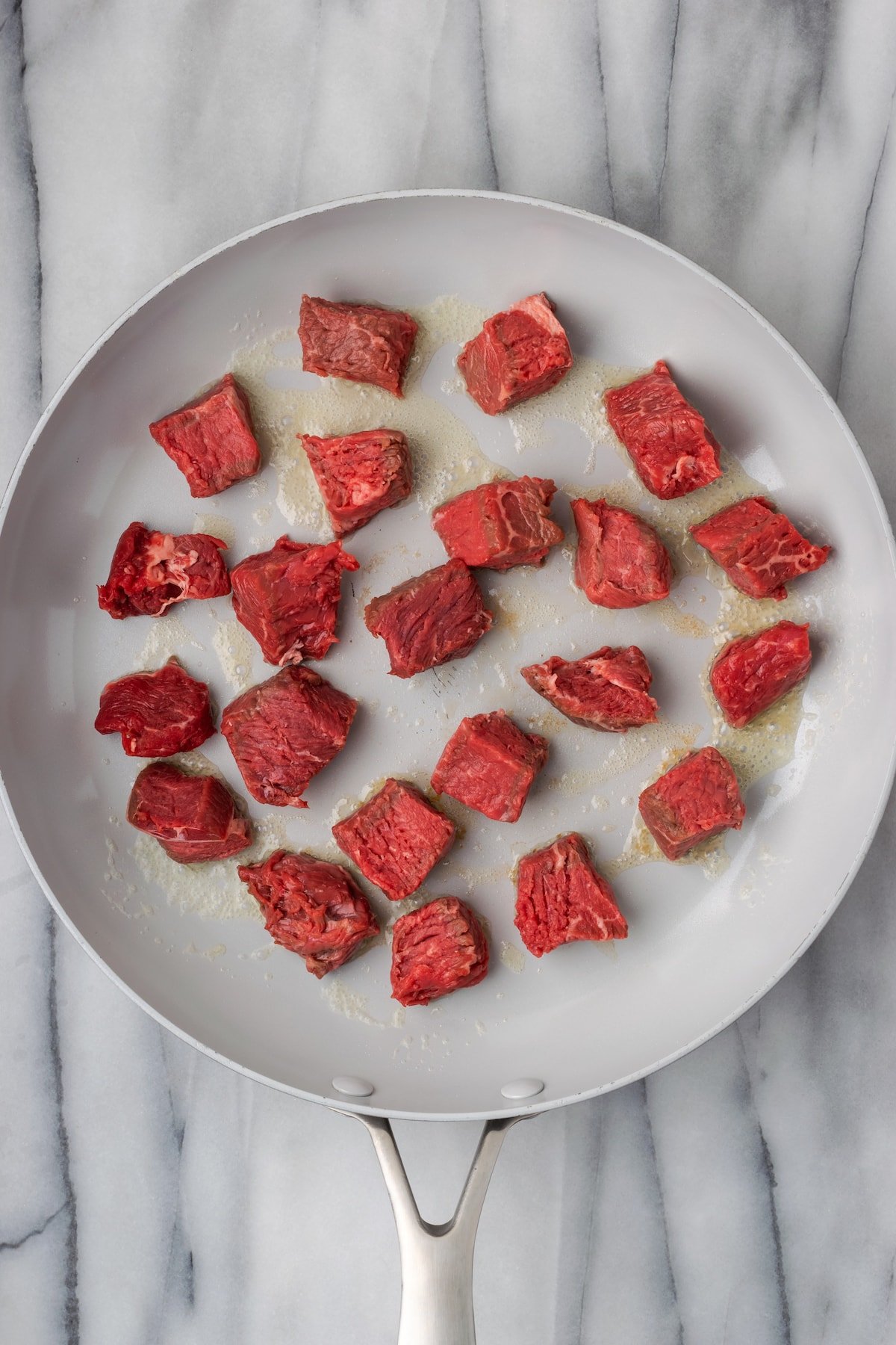 Cubes of raw steak in a skillet, not touching
