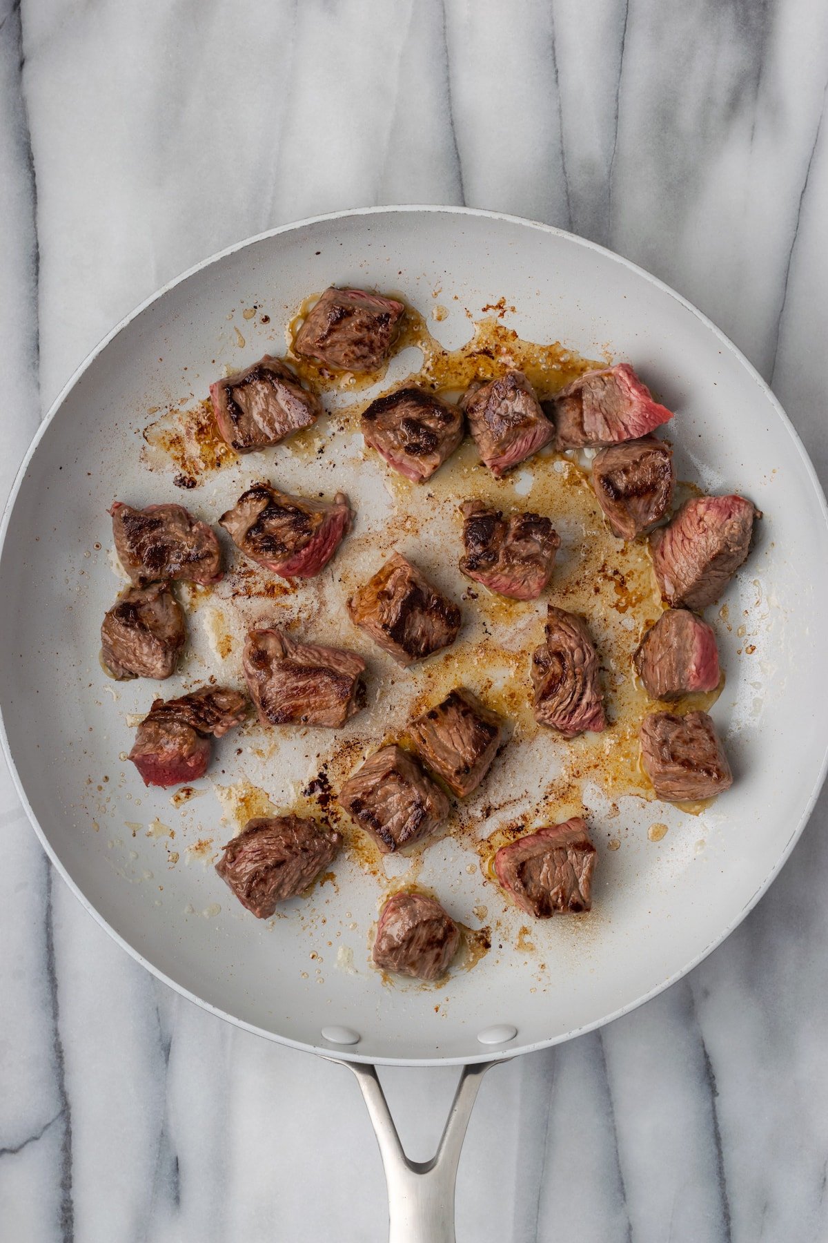 Steak bites searing in a skillet on multiple sides, not touching