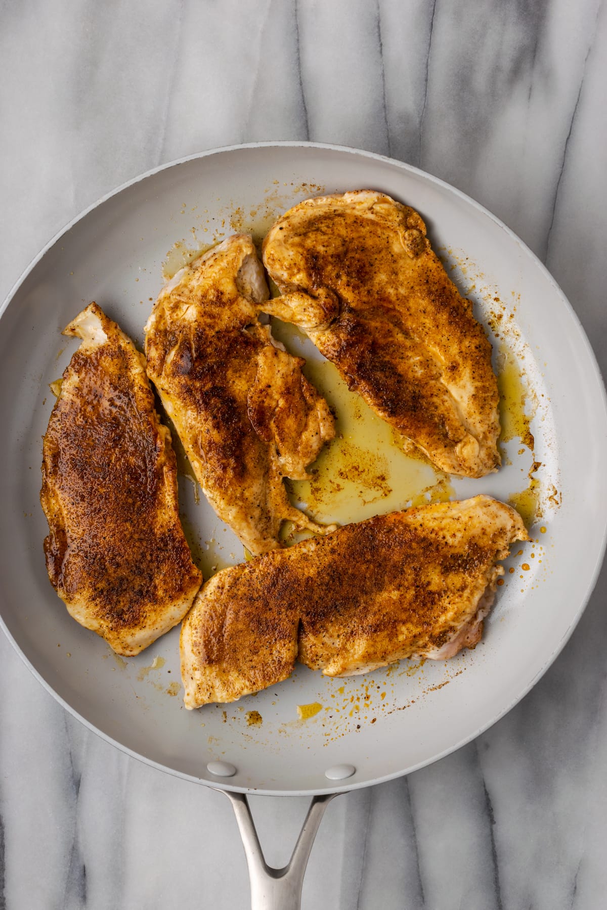 Overhead view of four seared chicken breasts in a skillet