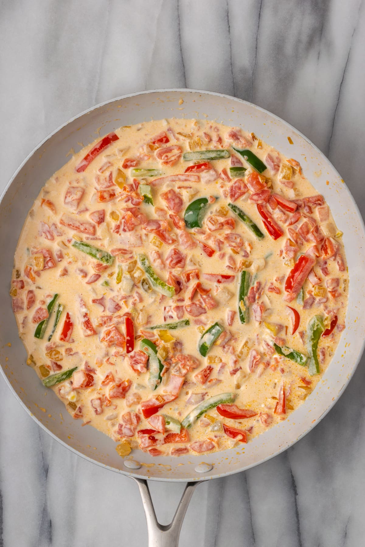 Overhead view of a cream sauce with red and green bell peppers in a skillet
