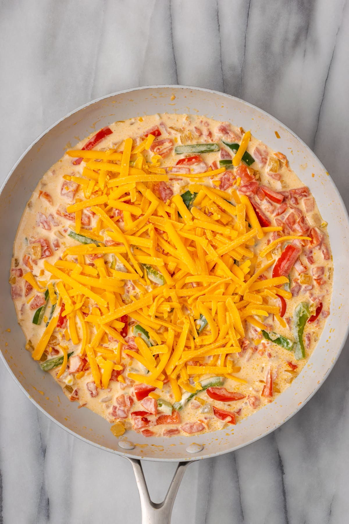 Overhead view of unmelted cheese on top of a sauce in a skillet