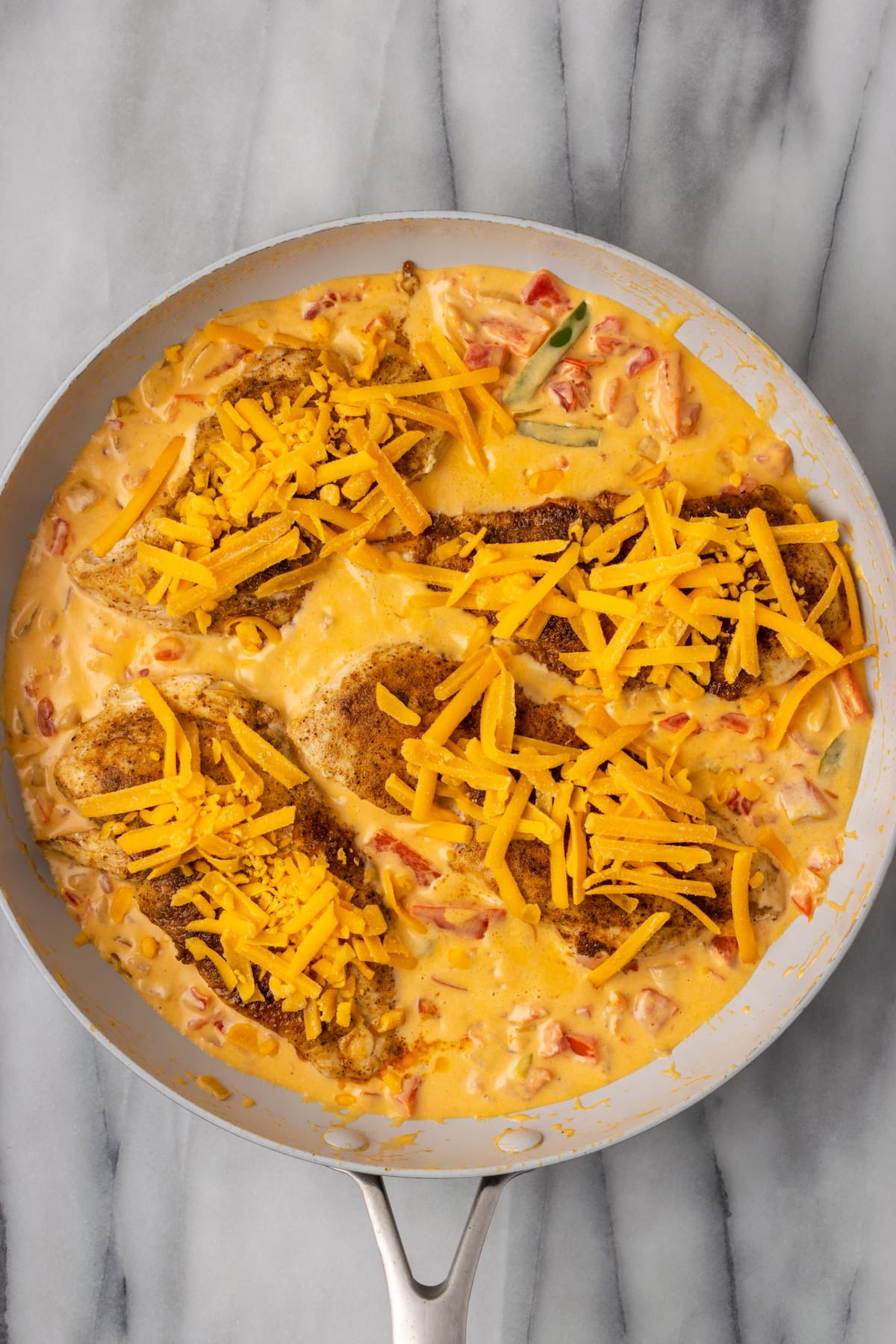 Overhead view of unmelted, shredded cheese on top of chicken breasts in a skillet
