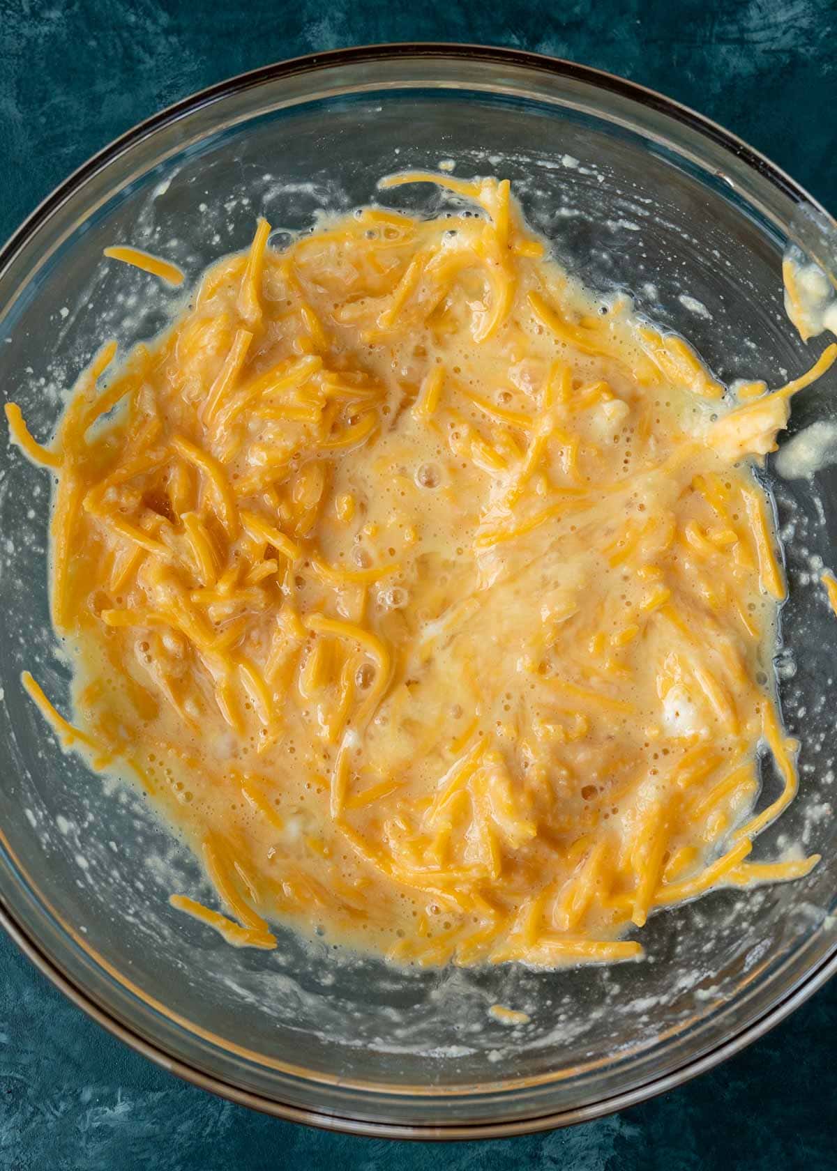 eggs whisked with almond flour, baking powder, and shredded cheese in a glass bowl