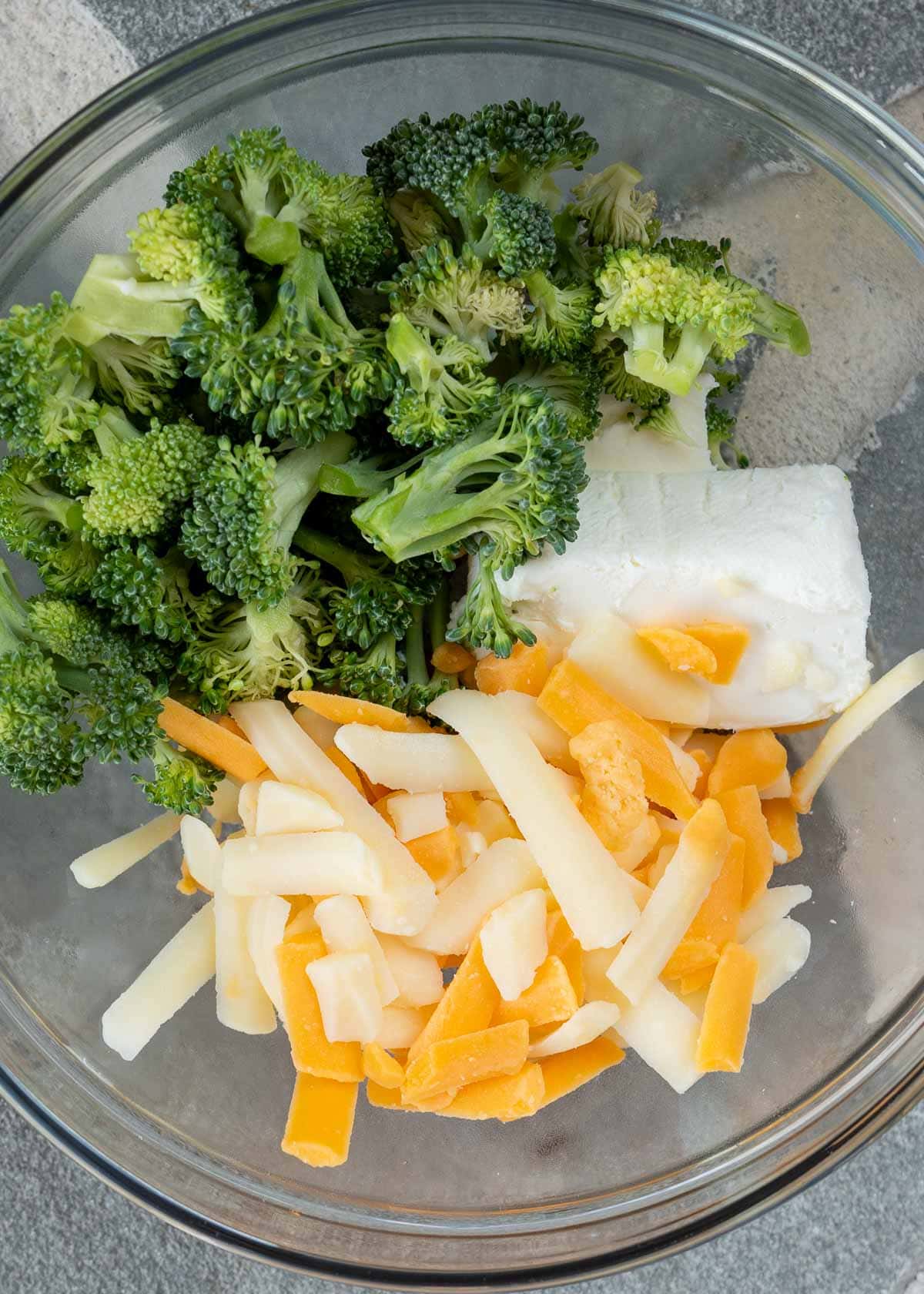 shredded cheese, softened cream cheese, and broccoli florets in a glass bowl