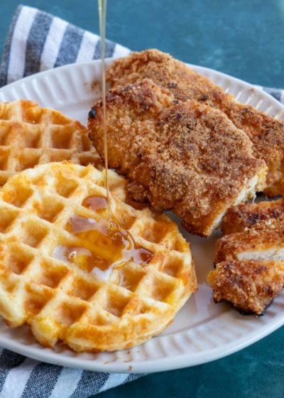 shot of sugar free maple syrup being poured on waffles with crispy chicken tenders