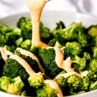 cheese sauce being poured on steamed broccoli