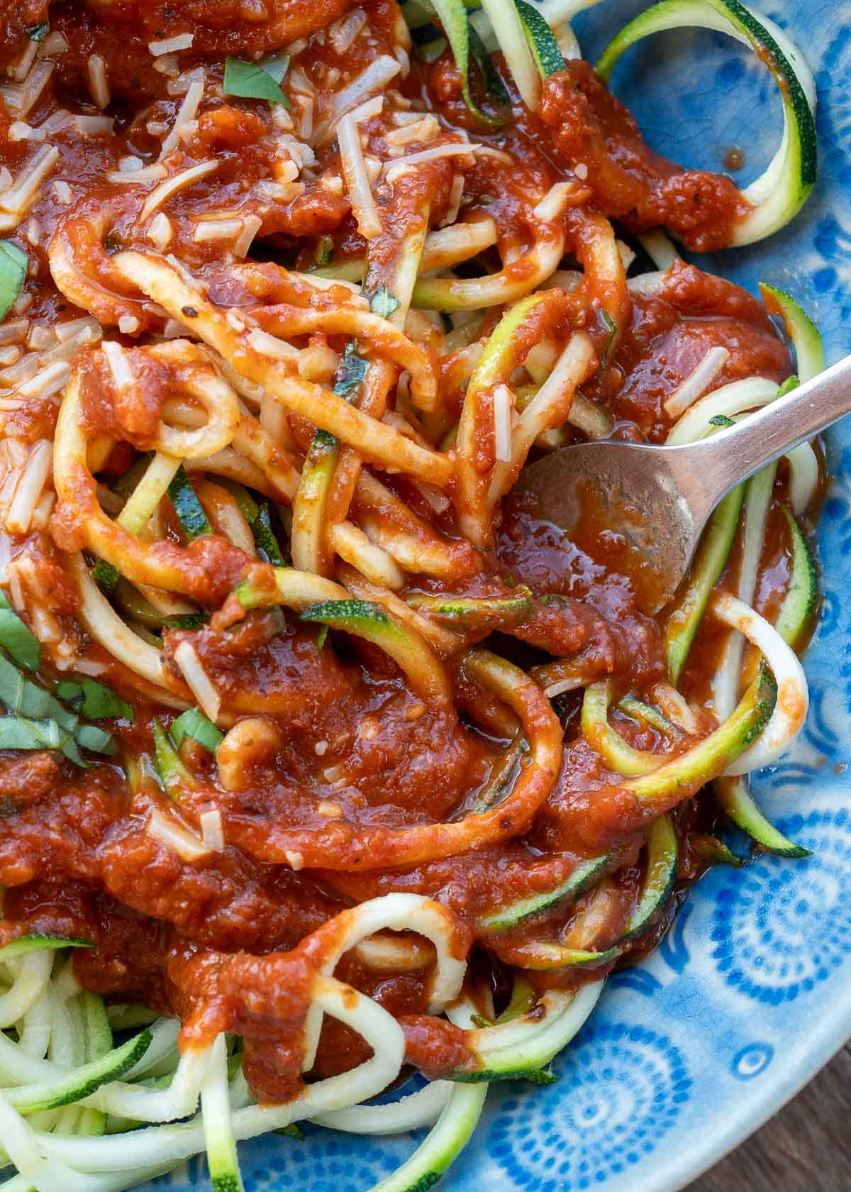 overhead shot of tomato sauce covering zoodles in a blue bowl