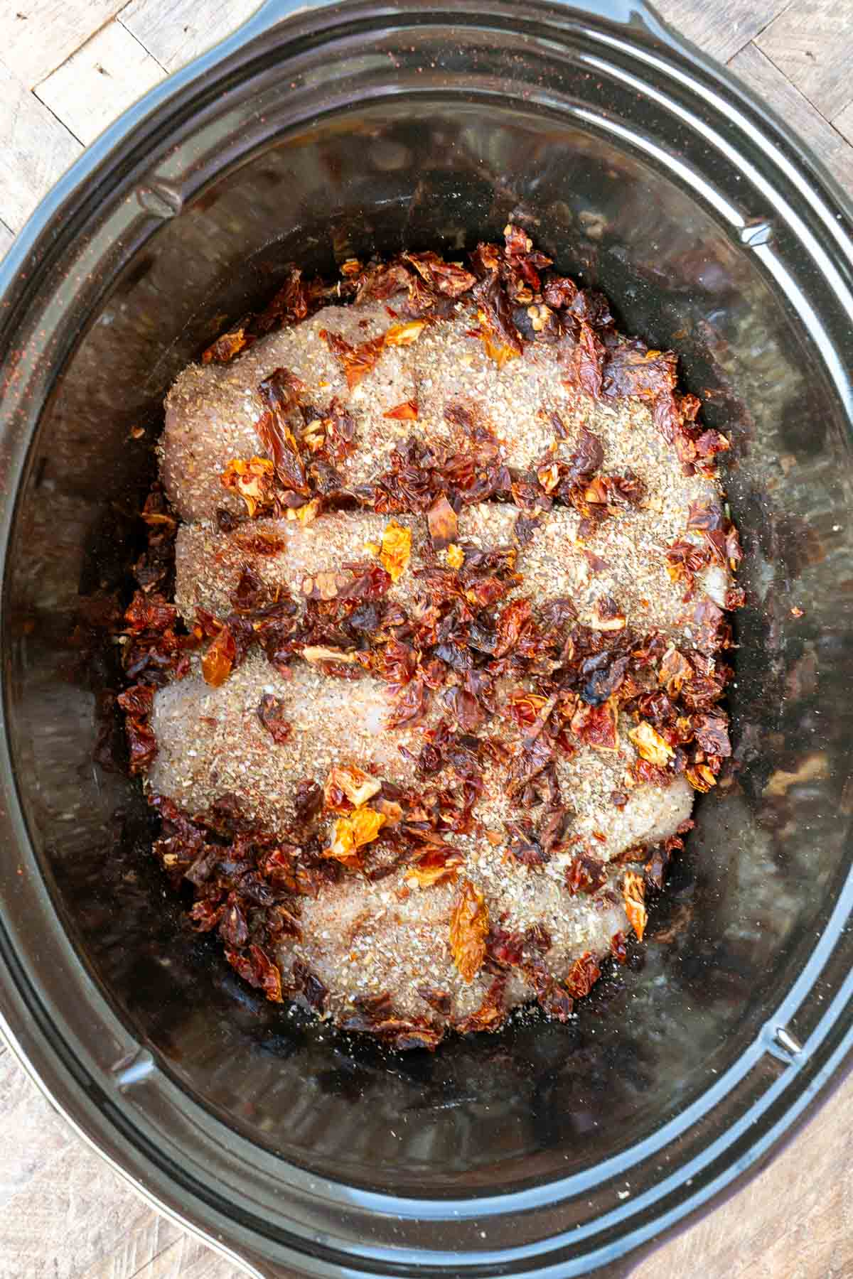 sun dried tomatoes being added to seasoned chicken in black crock pot