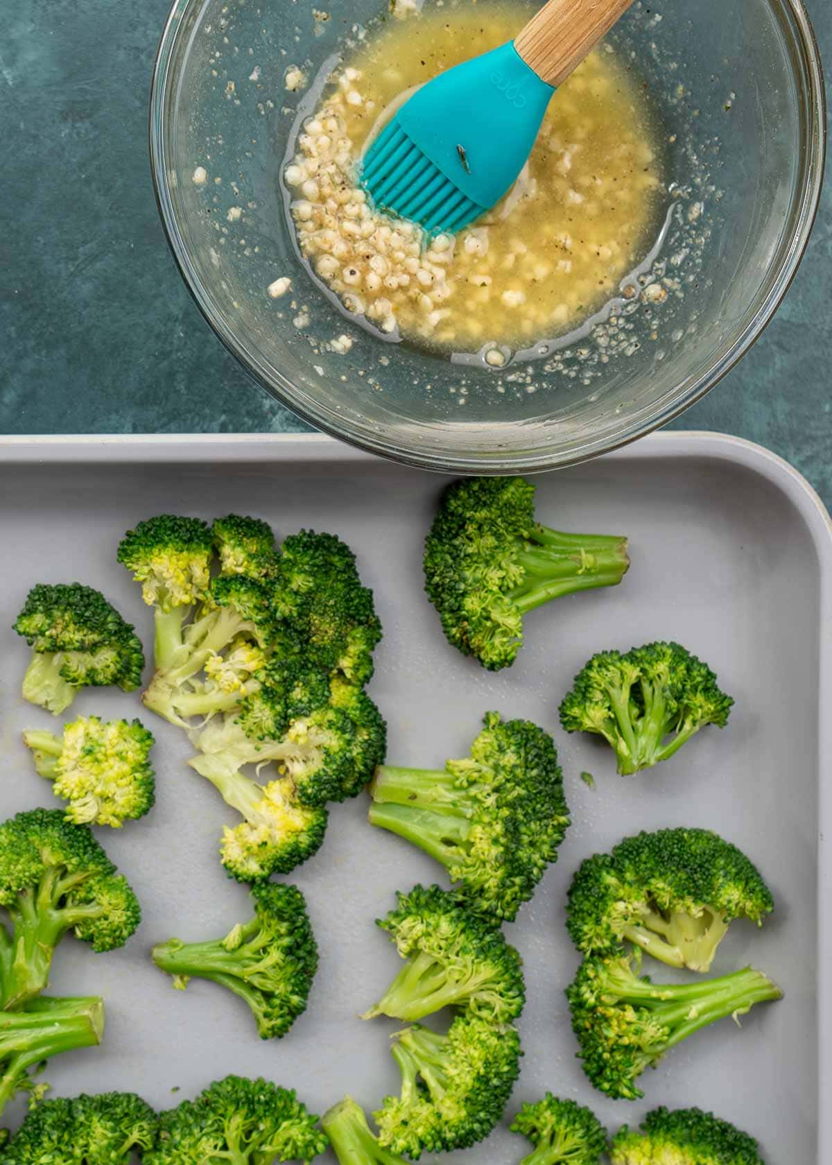 butter, garlic, and seasonings being mixed in a bowl beside a pan full of smashed broccoli