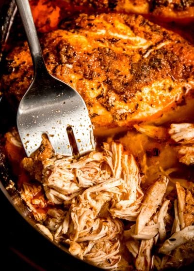 chicken breasts being shredded in black slow cooker