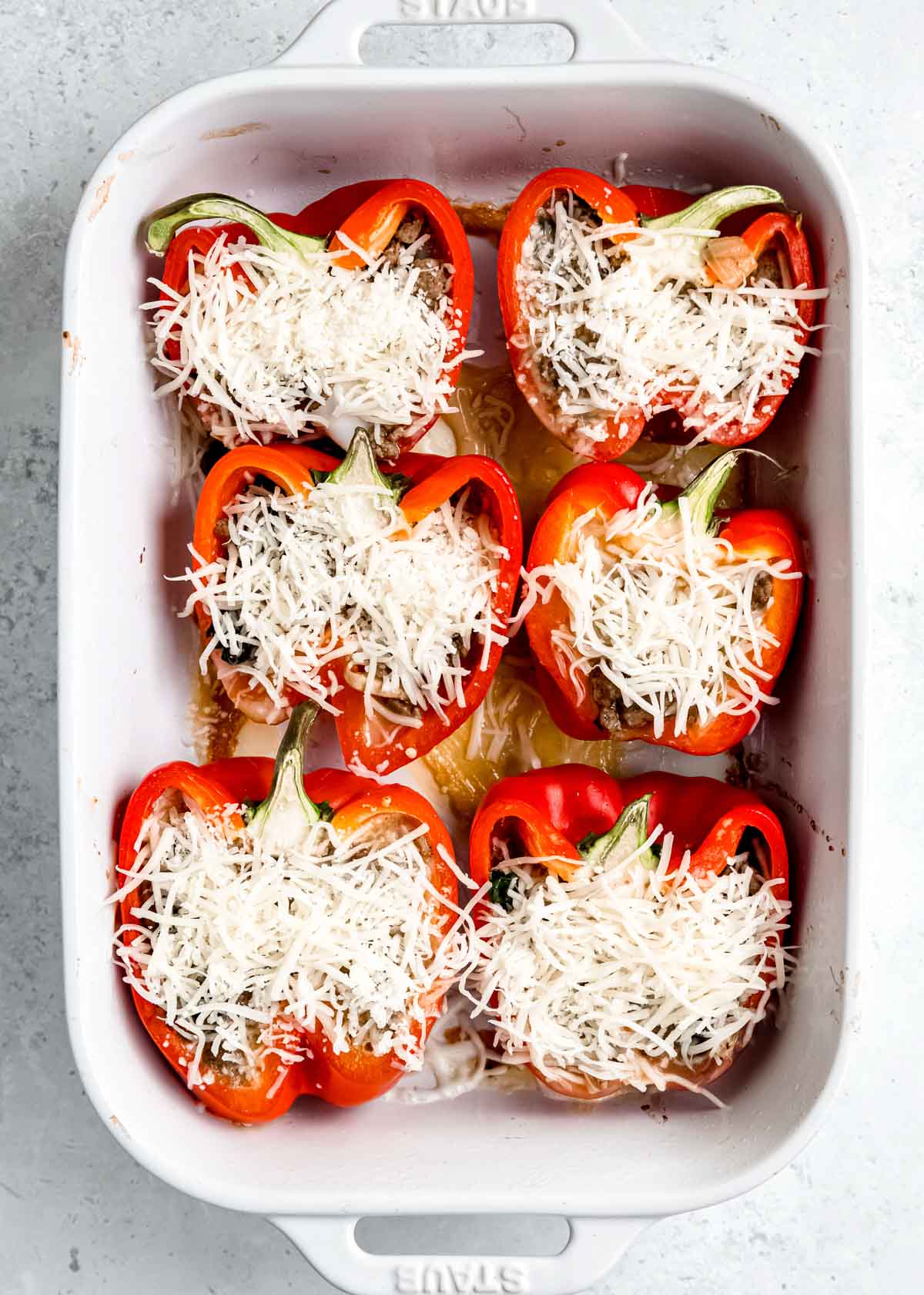cheese being added to stuffed bell peppers in baking dish