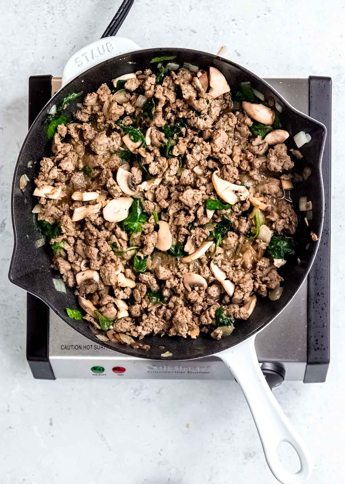 cooked breakfast sausage, mushrooms, and spinach in black skillet