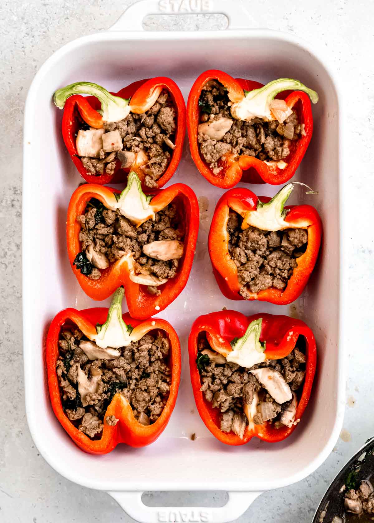 stuffing ingredients being added to stuffed bell peppers in baking dish
