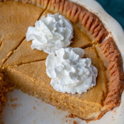 two sliced of pumpkin pie in a pumpkin pan with whipped cream