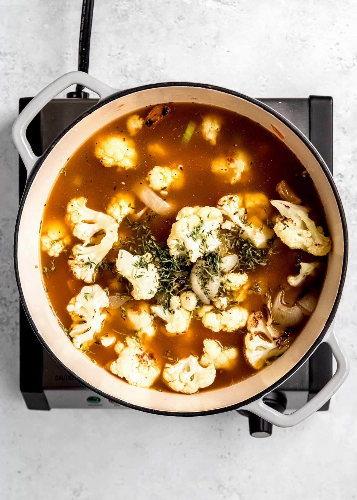 vegetable broth being added to cauliflower soup in dutch oven