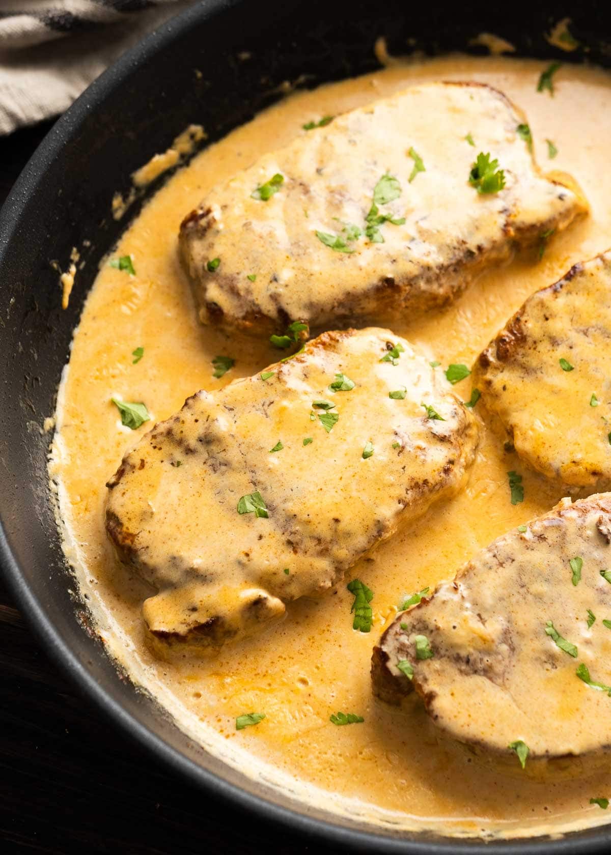 large skillet full of creamy cajun sauce and thick cut pork chops