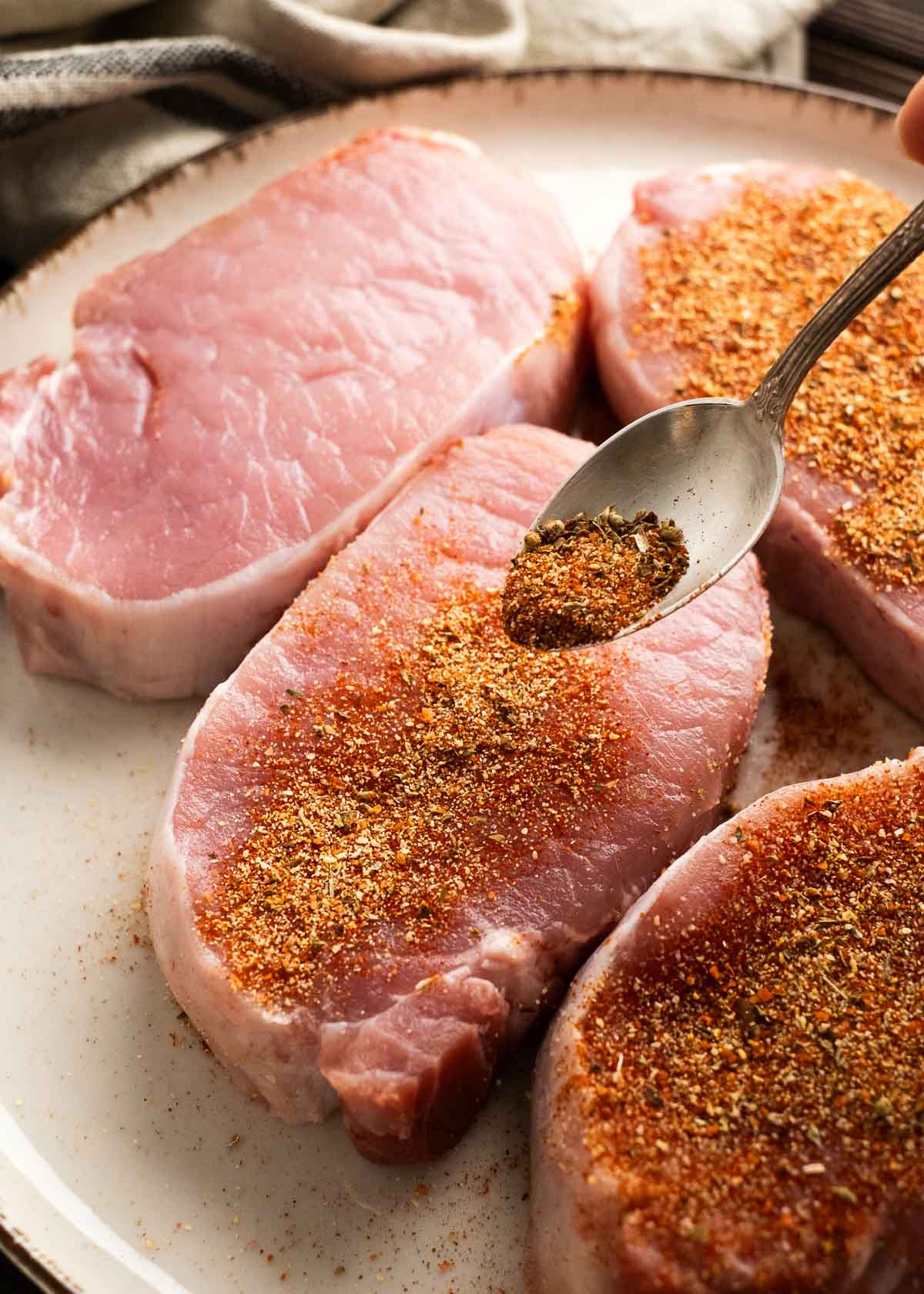 seasoning being sprinkled on four pork chops on a plate